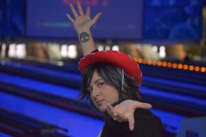 A woman wearing a red cowboy hat poses in a blue-lit bowling alley